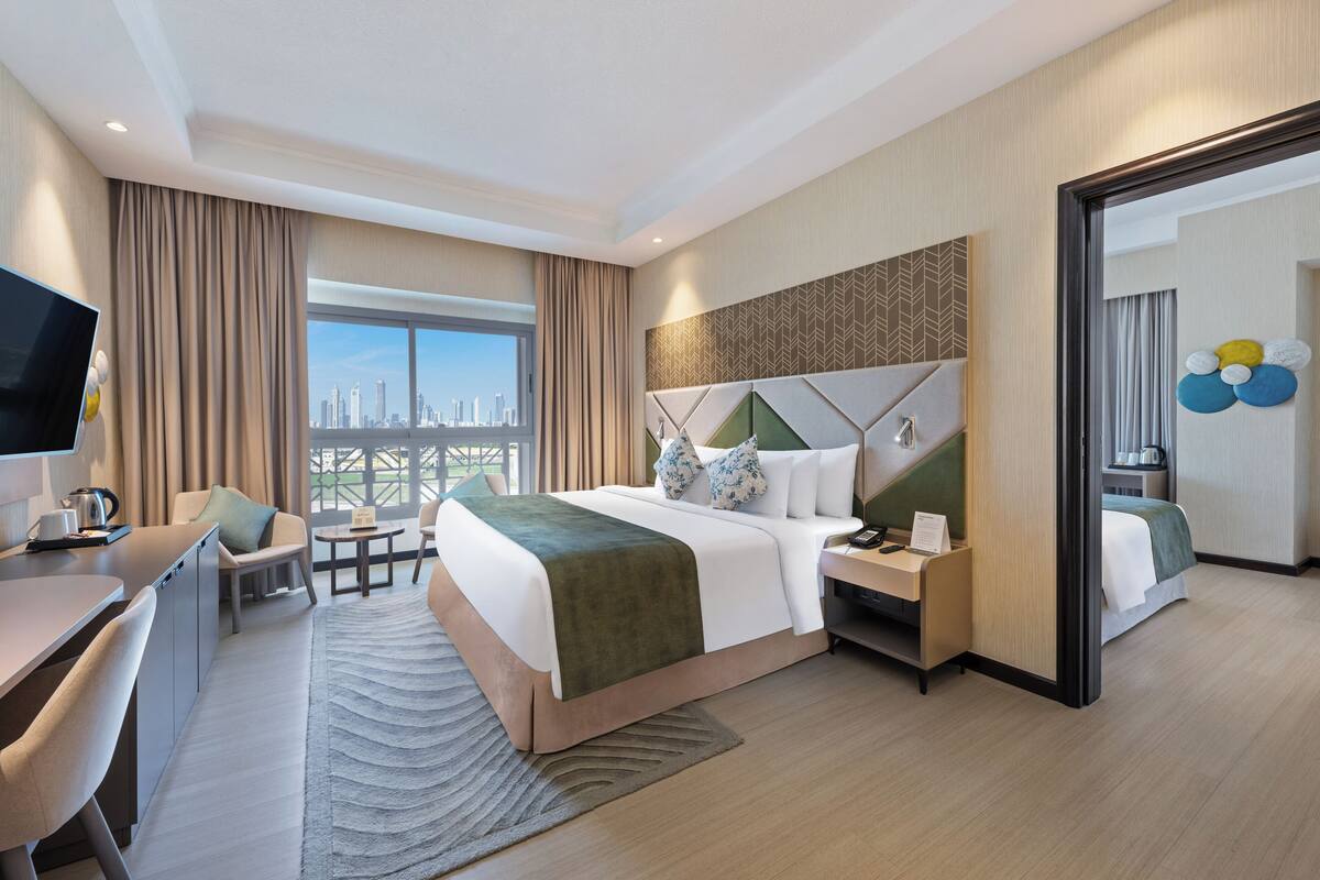 A hotel room with a bed, a desk, a chair, a TV, and a view of the city.
