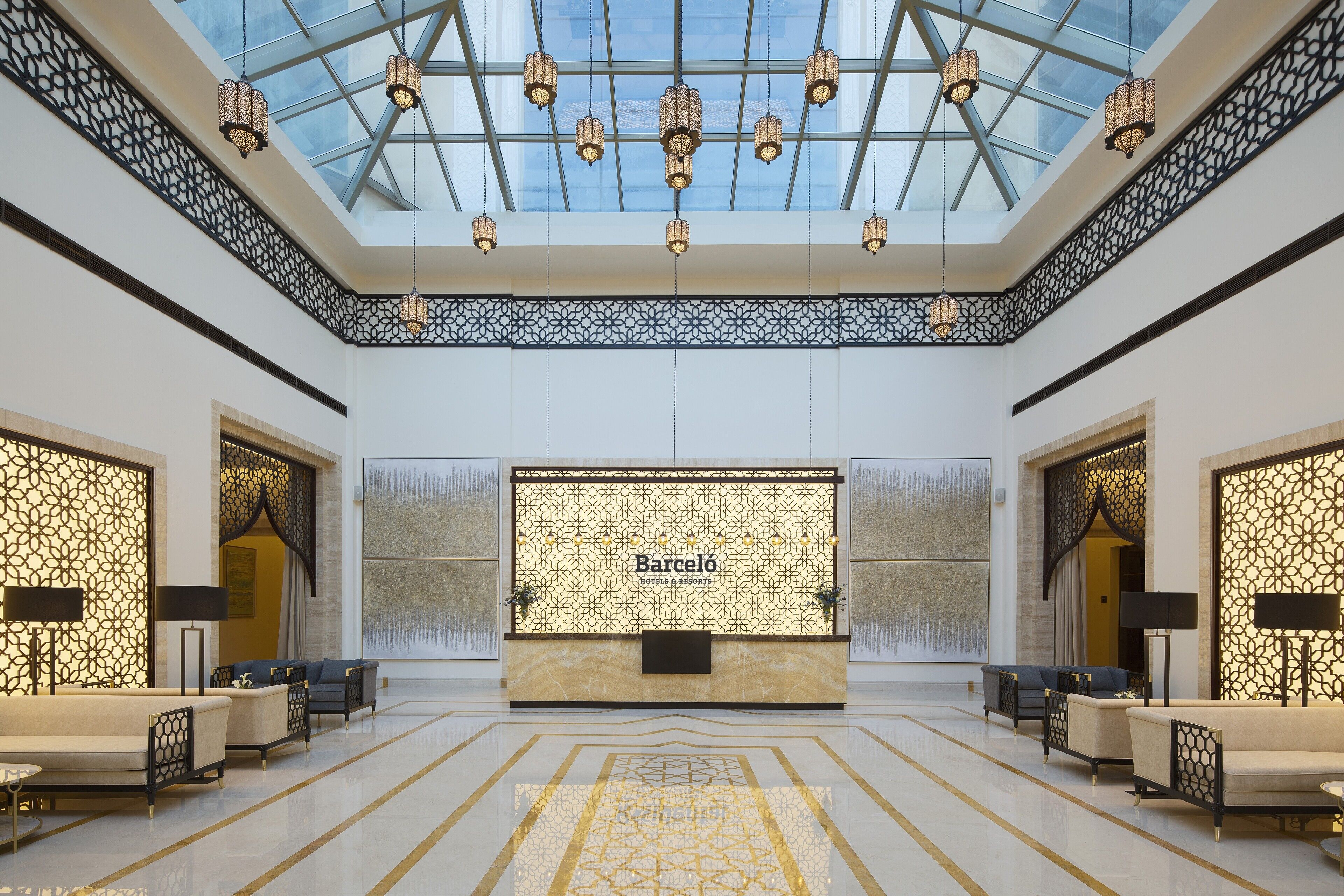 Un hall d’entrée spacieux avec un plafond haut, une verrière et un comptoir de réception portant l’inscription « Barcelo Hotel & Resorts ».