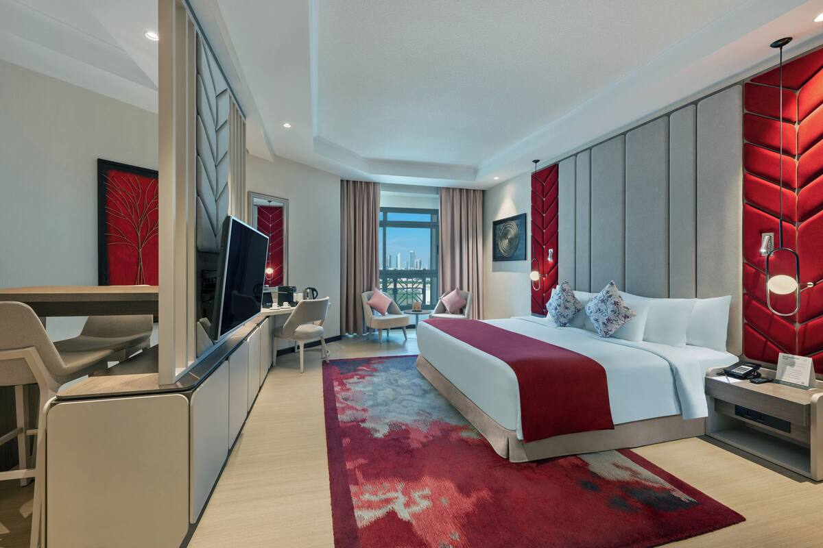 A modern hotel room with a large bed, a desk, a TV, and a city view.