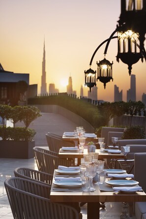 A restaurant with tables set for dining, overlooking a city skyline with a prominent tower. - Barceló Al Jaddaf (Dubai)