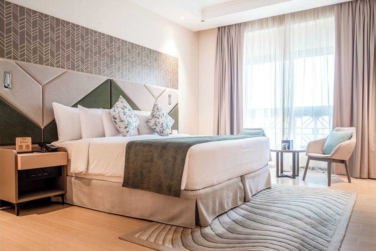 A modern hotel room with a large bed, a nightstand, a chair, and a view of the outdoors.