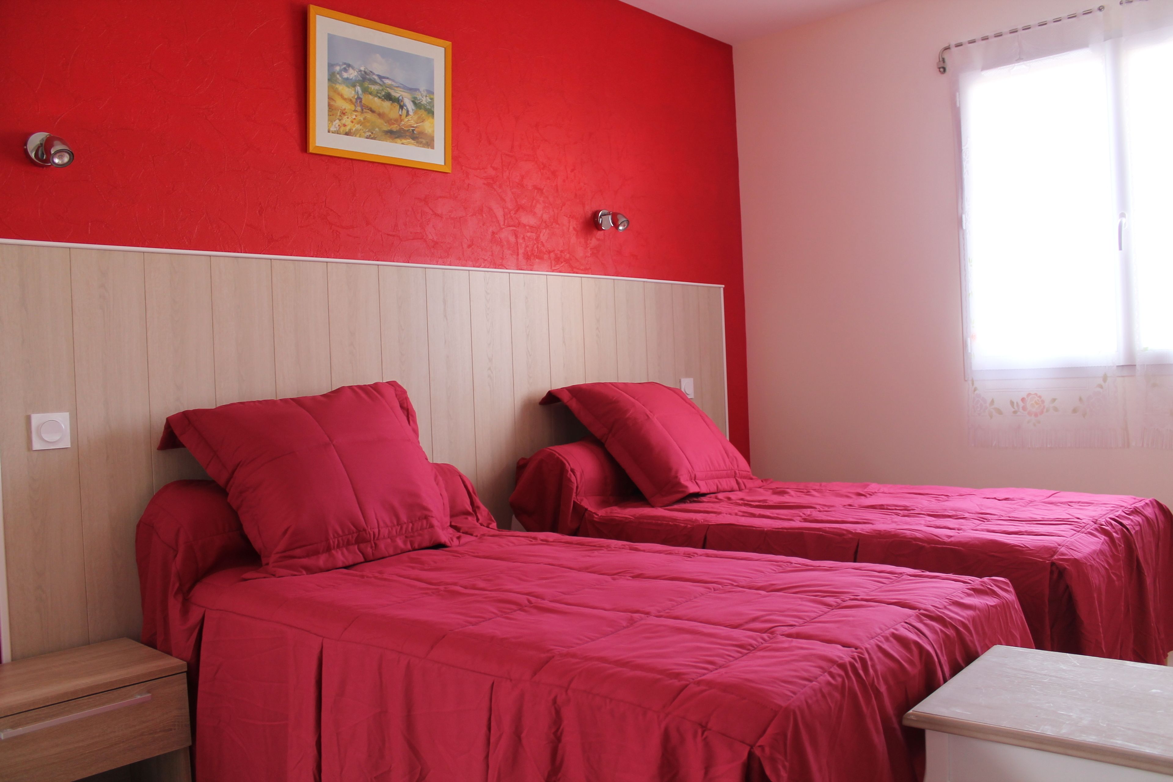 A room with two beds, each with red bedding, a wooden headboard, and a small bedside table.
