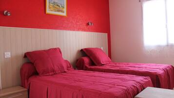 A room with two beds, each with red bedding, a wooden headboard, and a small bedside table.