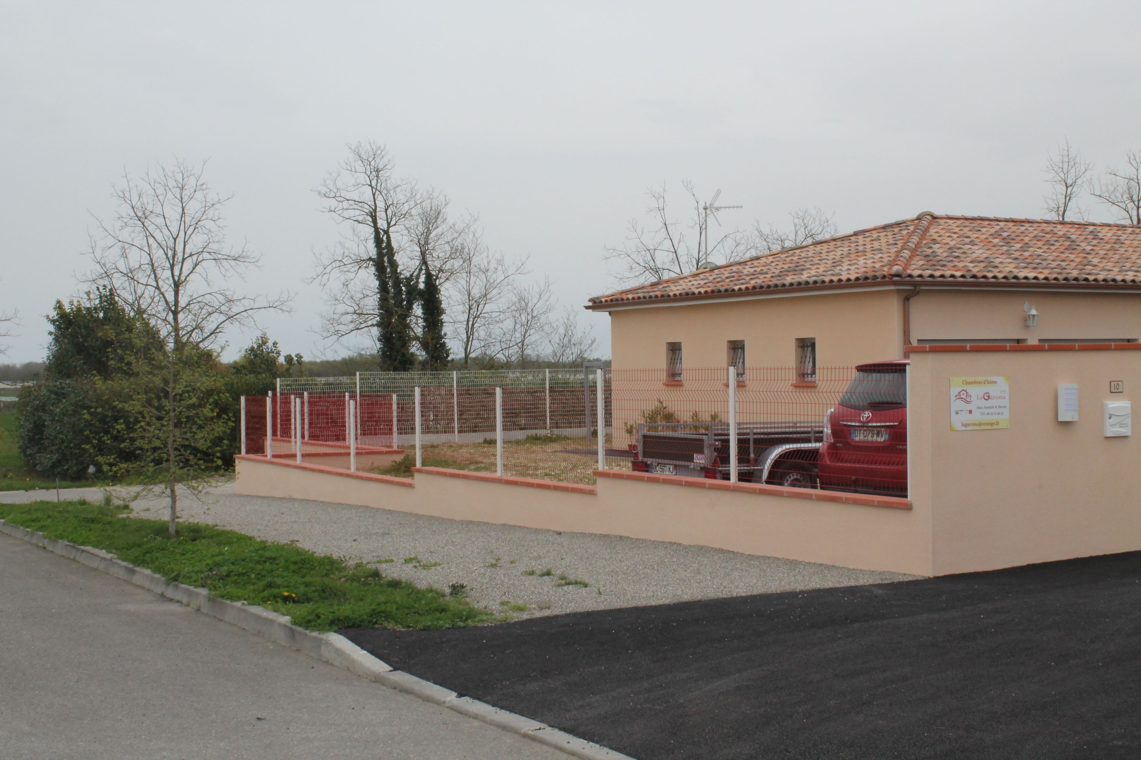 A building with a tiled roof, a fenced area, and a parked car.