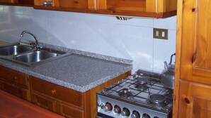 A kitchen with wooden cabinets, a granite countertop, a double sink, and a gas stove. - The Temple at Solebello (Morro D' Alba)
