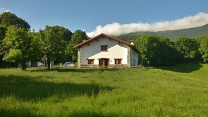 A white house with a red roof, surrounded by lush green grass and trees, with a mountain in the background. - Lenco House for 8 people (Zilbeti)