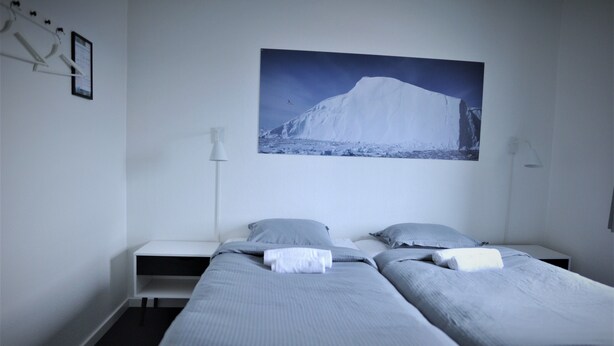 Ein Hotelzimmer mit zwei Einzelbetten, einem Nachttisch, einem Wandbild von einem Berg und einer stehenden Lampe.