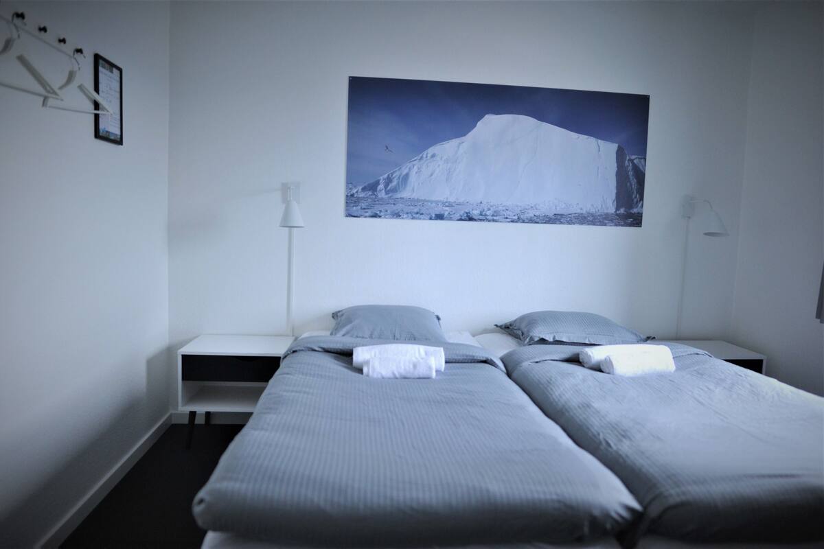Ein Hotelzimmer mit zwei Einzelbetten, einem Nachttisch, einem Wandbild von einem Berg und einer stehenden Lampe.