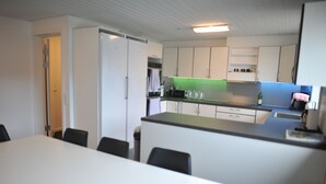 Eine moderne Küche mit weißen Schränken, einer schwarzen Arbeitsplatte und einer grünen Rückwand. Es gibt einen Essbereich mit einem weißen Tisch und schwarzen Stühlen.