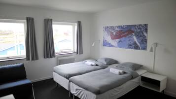 Habitación de hotel con dos camas, una ventana con cortinas, un radiador, un escritorio y un cuadro en la pared.