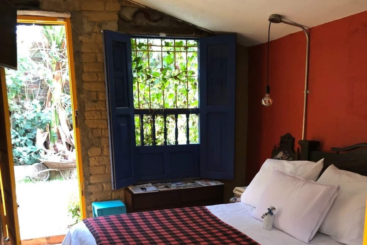 A bedroom with a checkered bedspread, a wooden headboard, and a window with blue shutters.