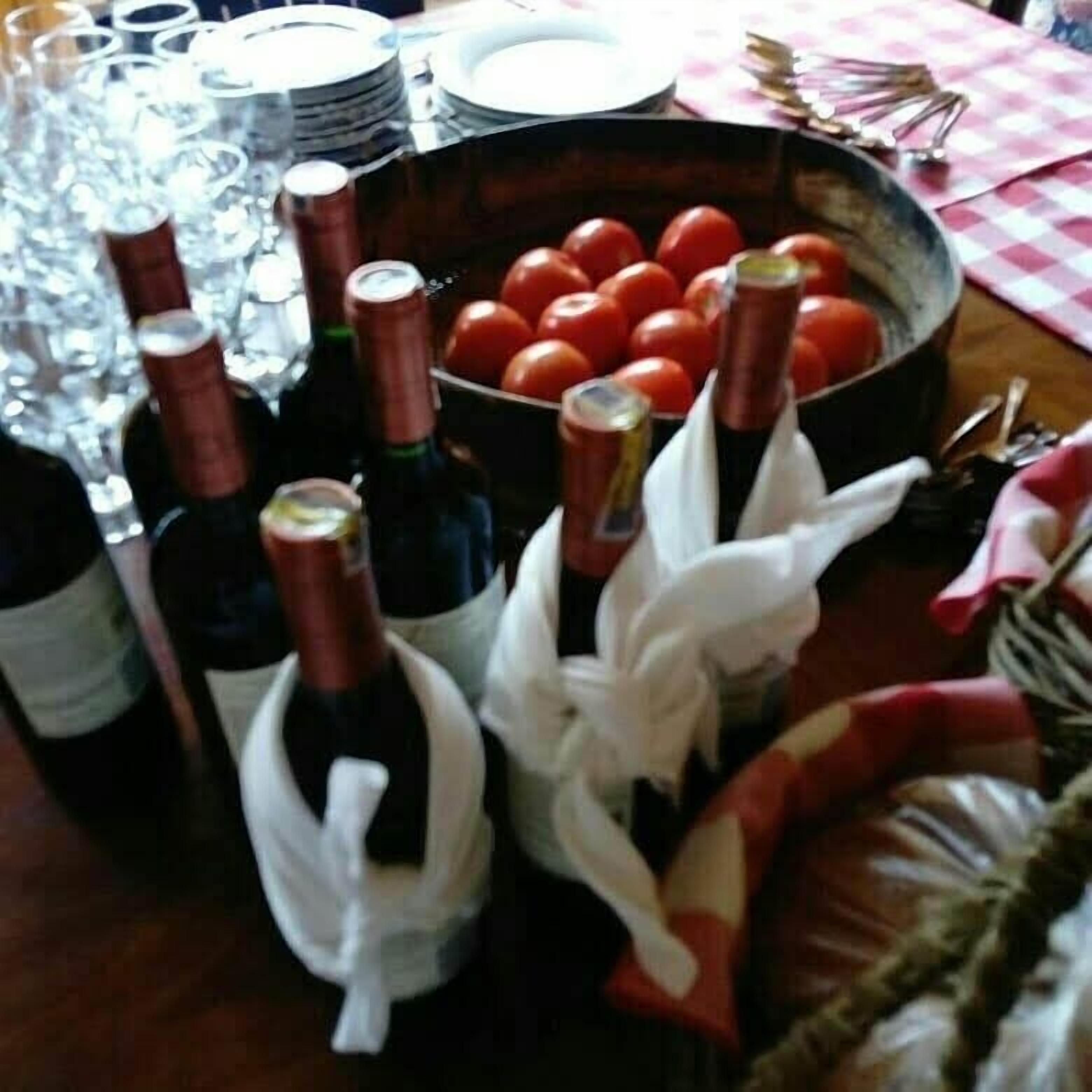 Una mesa con botellas de vino, copas y un bol de tomates.