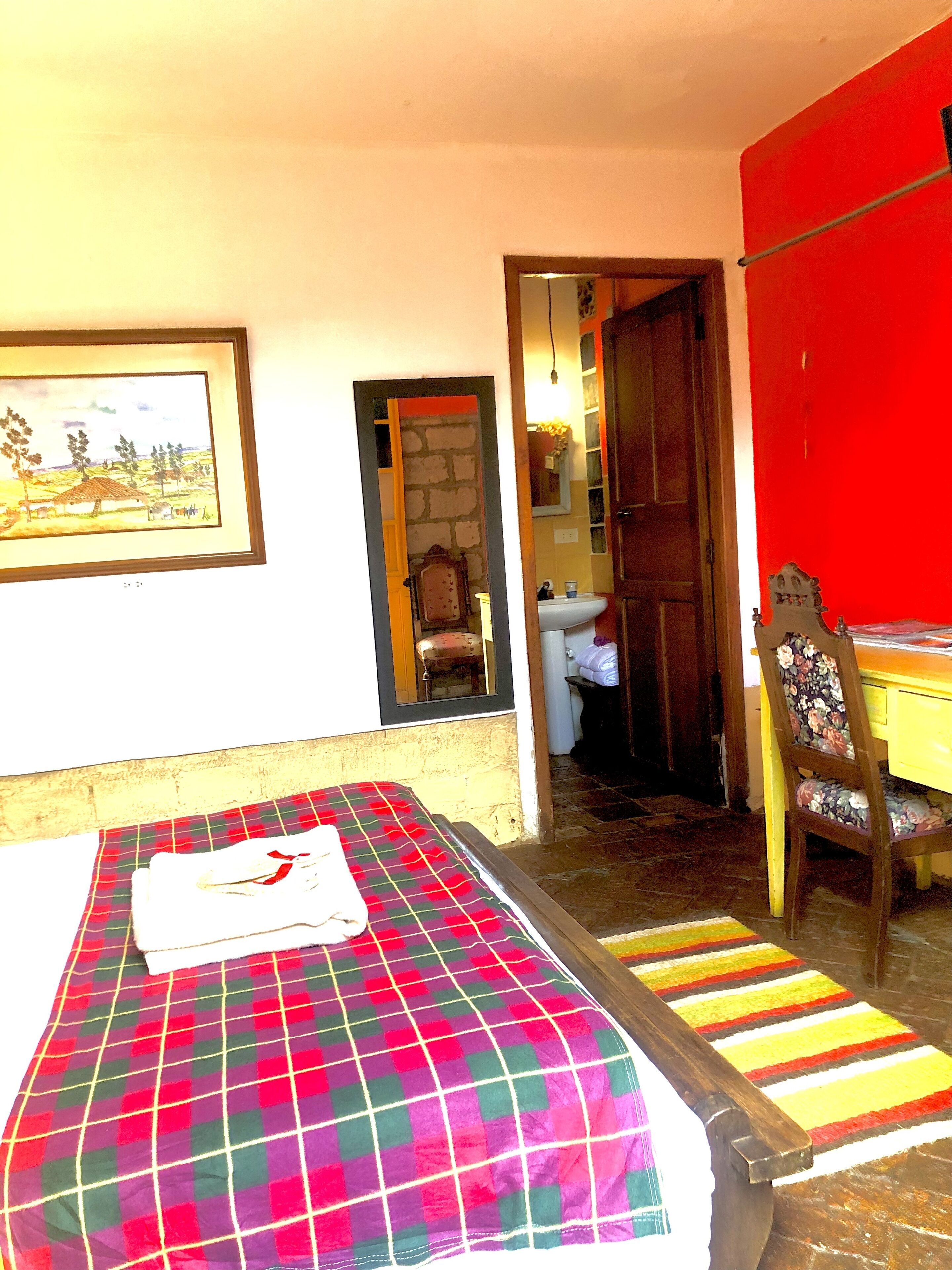 A room with a bed, a chair, a desk, and a bathroom visible through an open door.