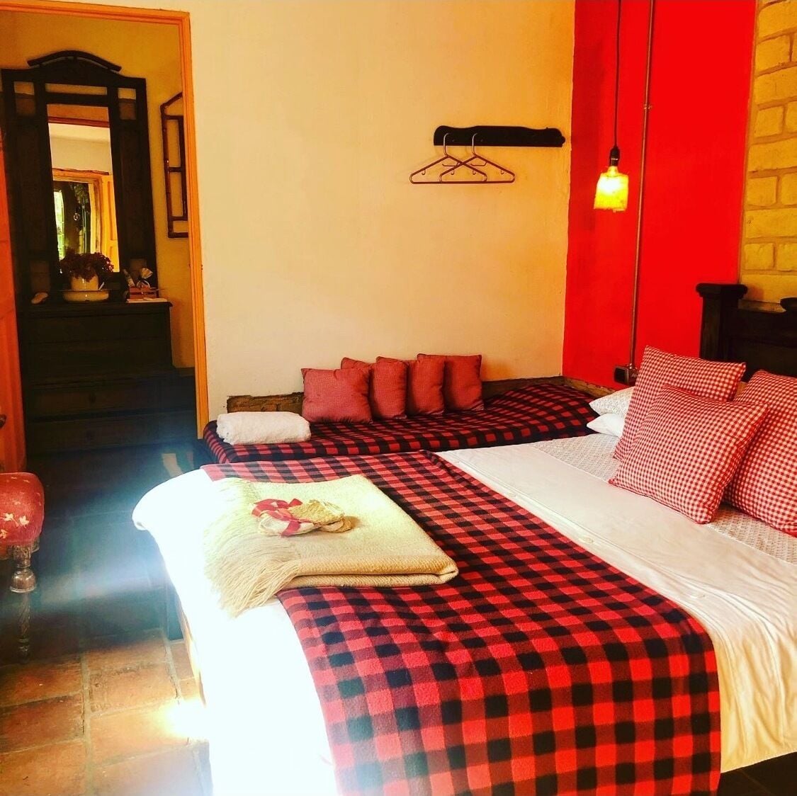 Habitación de hotel con colcha a cuadros, almohadas rojas y una lámpara colgante.