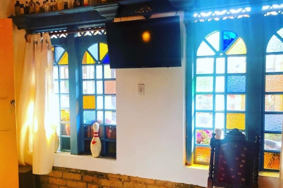 A room with a bed, a chair, a TV, and windows with colorful stained glass.