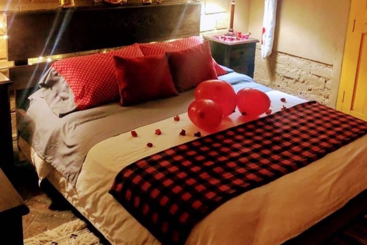 A bedroom with a bed, red pillows, a checkered blanket, and balloons.