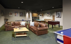 Een kamer met twee bruine leren banken, een pooltafel, een tafelvoetbaltafel en een pingpongtafel.