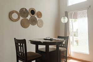 A dining area with a round table, two chairs, and a wall adorned with woven placemats.