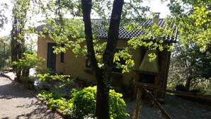 Um edifício rústico de pedra com telhado de telhas, rodeado por vegetação exuberante e árvores.
