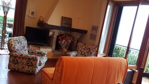 Uma sala de estar com lareira, poltronas florais, um sofá e uma televisão.