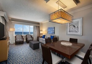 A hotel room with a large window, a dining table, and a sofa.