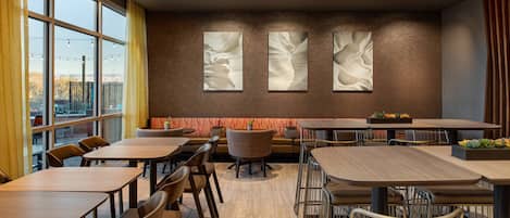 Un restaurante moderno con mesas y sillas de madera, ventanas amplias y arte abstracto en las paredes.