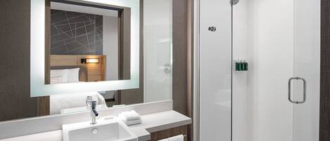 A modern bathroom with a large mirror, a sink, and a glass-enclosed shower.