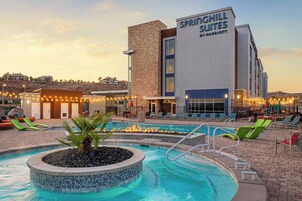 A hotel with a swimming pool, lounge chairs, and a fire feature.
