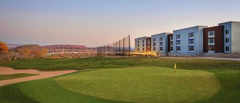 A golf course with a flag, a building with multiple floors, and a distant mountain range.