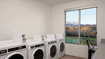 A laundry room with three front-loading washing machines, a large window with a view of mountains and trees, and a black chair.