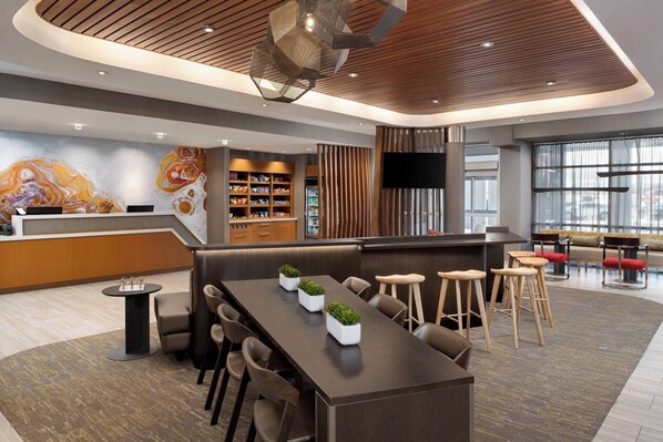 A modern hotel lobby with a reception desk, seating area, and a large mural.