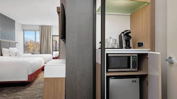 A hotel room with a bed, a small kitchenette with a microwave, and a refrigerator.