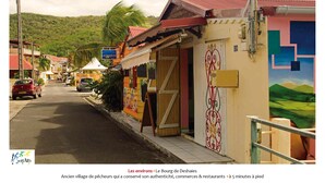 A street view of a village with traditional buildings, a sign for a restaurant, and a mural on a building. - Villa O Jardin d'Alice (Deshaies)