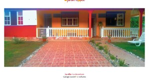 A colorful villa with an open garage and two vehicles parked outside. - Villa O Jardin d'Alice (Deshaies)