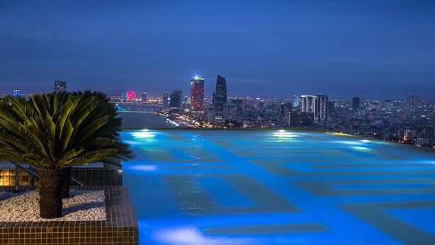 A cityscape at night with illuminated buildings and a river with geometric patterns. - Citadines Blue Cove Danang (Da Nang)