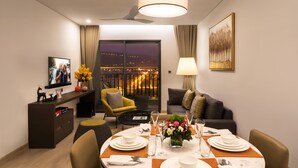 A modern hotel room with a dining area, a sofa, a TV, and a balcony with a city view. - Citadines Blue Cove Danang (Da Nang)