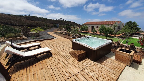 A wooden deck with lounge chairs and a hot tub, surrounded by landscaped gardens and a hillside. - ANCON 116, LUXURY VILLA & ESTATE IN SOUTH TENERIFE. (Santa Cruz de Tenerife)