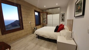 A modern bedroom with a large bed, a bedside table, a radiator, and a window with a view of a mountain. - ANCON 116, LUXURY VILLA & ESTATE IN SOUTH TENERIFE. (Santa Cruz de Tenerife)