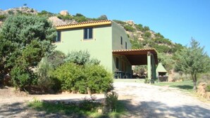 Un bâtiment à deux étages, doté d’une façade verdoyante et d’un toit en tuiles, entouré de verdure et surplombant un ciel dégagé.
