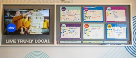 A bulletin board with various handwritten notes and a TV screen displaying a man playing with a stack of boxes.