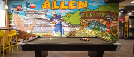 A pool table with a mural in the background featuring a football player, a bridge, and a river.