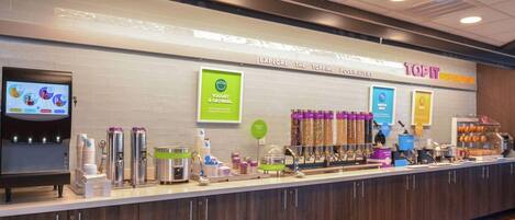 A breakfast bar with yogurt and oatmeal options, waffle and pancake makers, and a coffee machine.