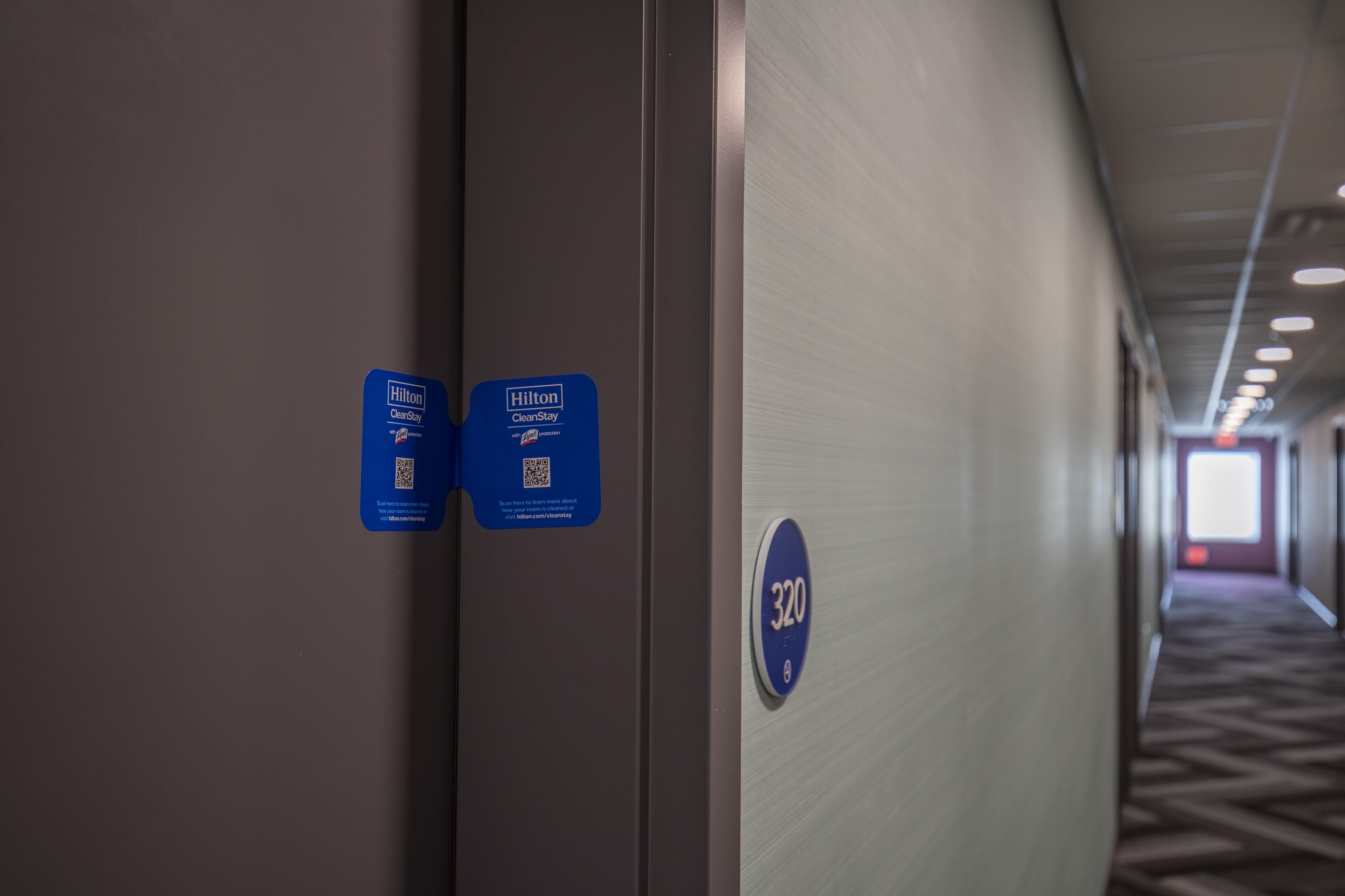 A hallway with a blue sign indicating room number 320, a QR code, and a Hilton CleanStay sign.