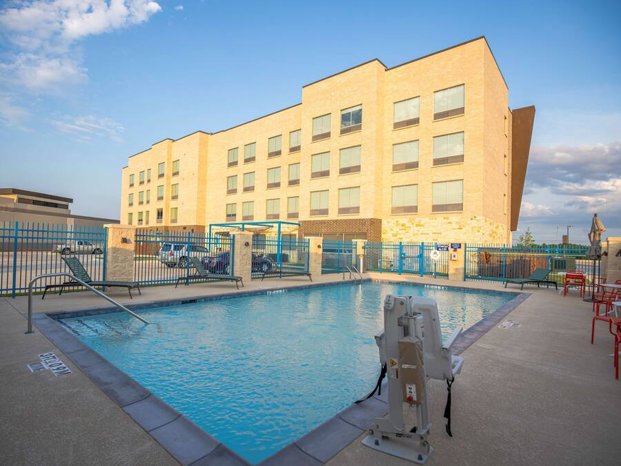 A swimming pool with a blue water feature, surrounded by a blue fence, and a building with multiple windows in the background.