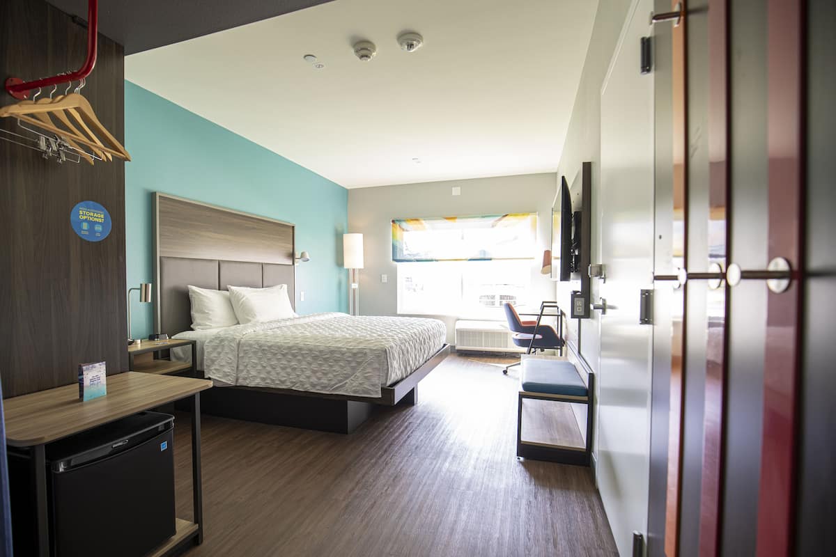 A hotel room with a bed, desk, and a small refrigerator.