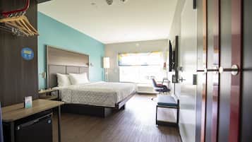 A hotel room with a bed, desk, and a small refrigerator.