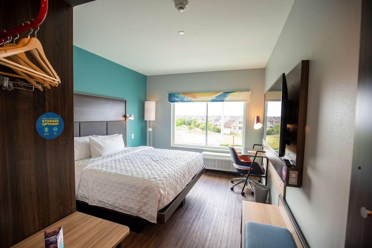 A hotel room with a bed, a desk, a chair, a TV, and a window with a view.