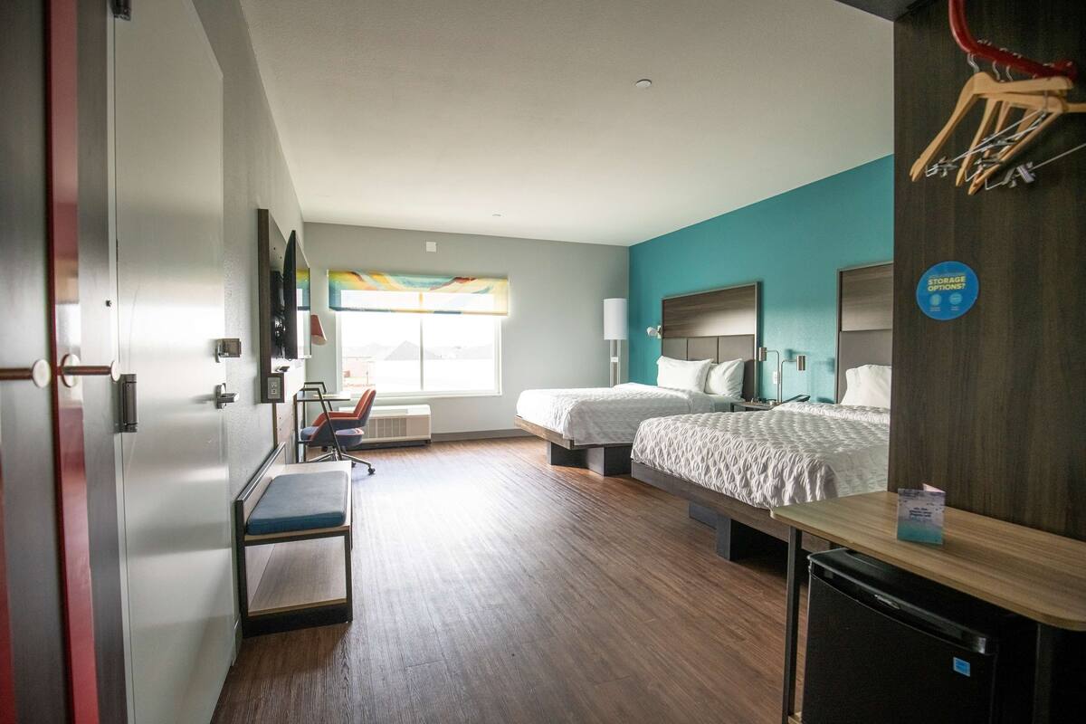A hotel room with two beds, a desk, a chair, a TV, and a window with a view.