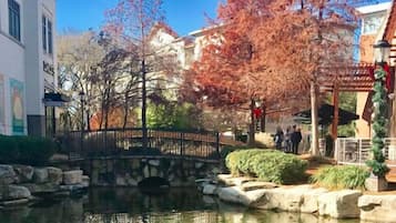 A stone bridge over a pond with autumn foliage, a restaurant with outdoor seating, and a building with a mural.