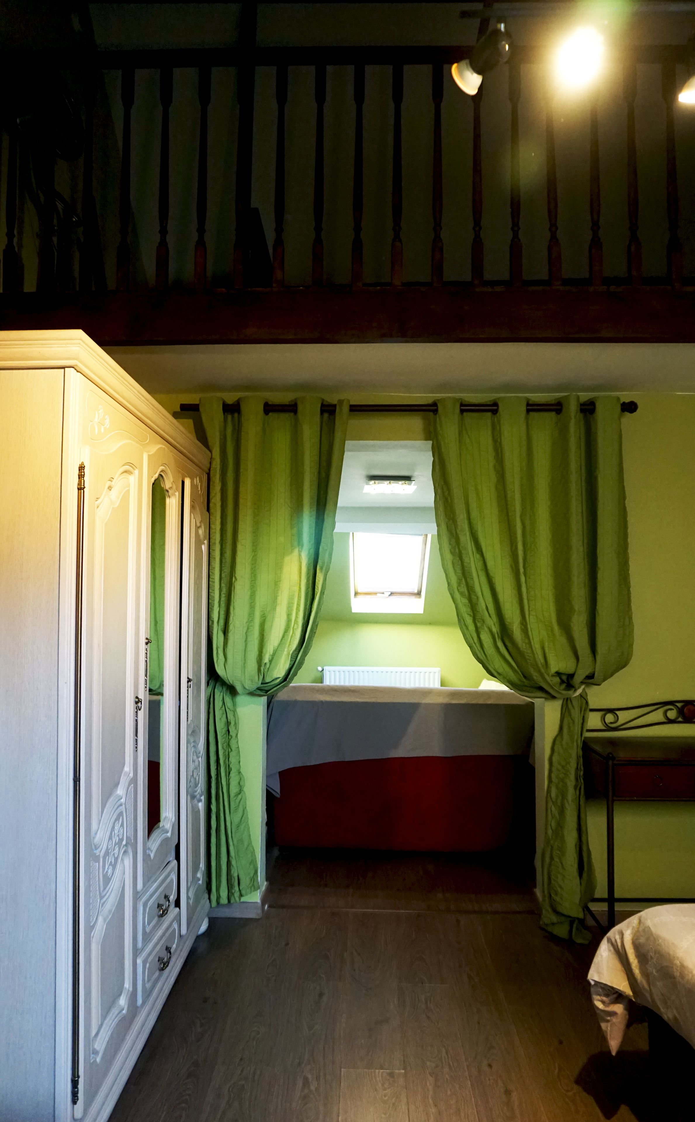 Une chambre avec un lit superposé, une armoire, une fenêtre avec des rideaux et une lucarne.